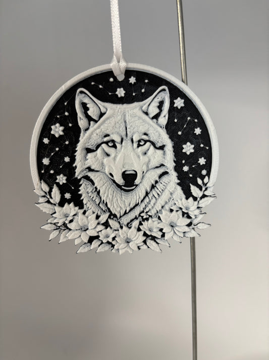 A round hanging ornament featuring a detailed black and white illustration of a wolf's face surrounded by stars and flowers, suspended by a white ribbon against a neutral gray background.