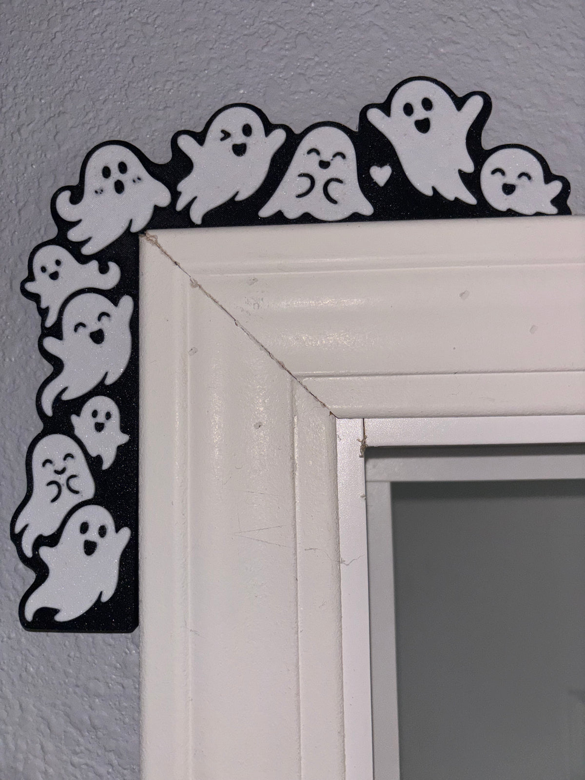 White ghost figures on black L-shaped decoration resting on the top-left corner of a white door frame.